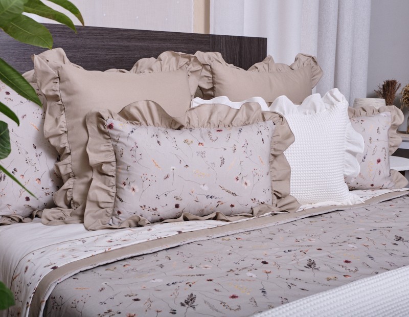 Funda de cojín con fondo en color beige arena y estampado de flores. Diseño lencero terminado en volante.