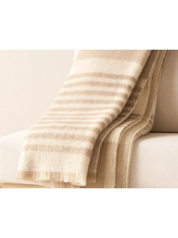 Manta plaid Sena de Clara Vidal doblada sobre sofá en tonos beige. Ampliada